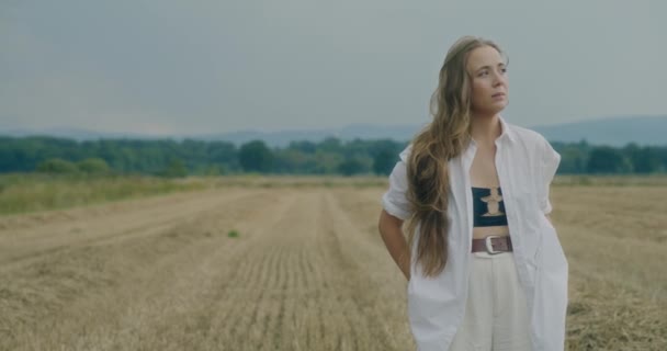 一个悲伤的年轻女子站在田野里 面对天空 慢慢地扭转眼望向远方 — 图库视频影像