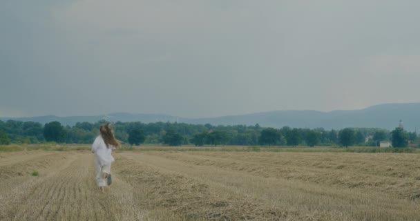 スローモーションショット 空に向かってフィールドで走っている間 肩越しに見えるケアフリーの若い女性 — ストック動画