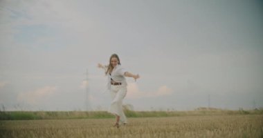 Yavaş çekim mutlu genç kadın koşuyor ve gökyüzüne karşı sahada eğleniyor