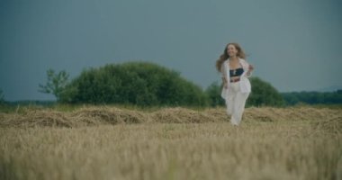Yavaş çekim mutlu genç kadın gökyüzüne karşı çimenlerde koşarken eğleniyor