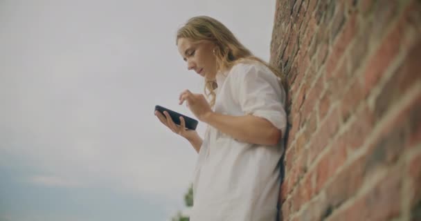 Tuğla Duvara Yaslanırken Akıllı Telefonu Kaydıran Genç Bir Kadının Yavaş — Stok video