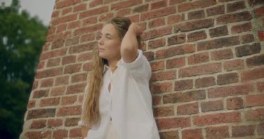 Yavaş çekim, eli saçları tuğla duvara dayanmış düşünceli bir kadın.