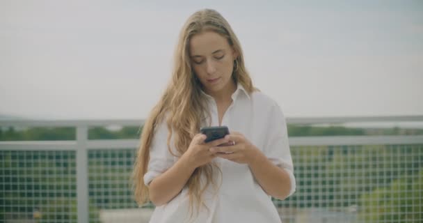Güzel Bir Genç Kadının Gökyüzüne Karşı Dururken Cep Telefonuyla Mesajlaşmasını — Stok video