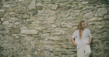 Taş duvara yaslanmış güzel genç bir kadının yavaş çekim sahnesi.
