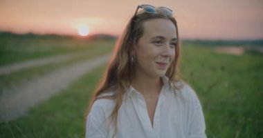 Gün batımında çayırda gökyüzüne karşı hayal kuran güzel genç bir kadının yavaş çekim görüntüleri.