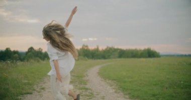 Yavaş çekim kaygısız genç bir kadın kollarını açmış gökyüzüne karşı yaylalar üzerinde koşarken.