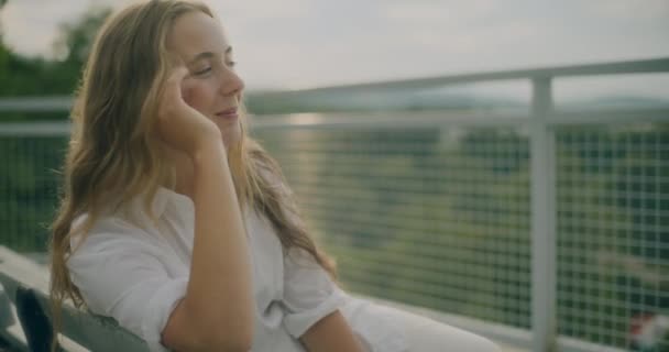 ベンチに座っている間に髪を気遣う金髪の女性を笑顔にするスローモーションショット — ストック動画