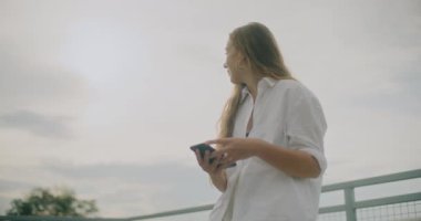 Çekici genç bir kadının cep telefonunu gökyüzüne karşı kullanmasının yavaş çekim görüntüleri.