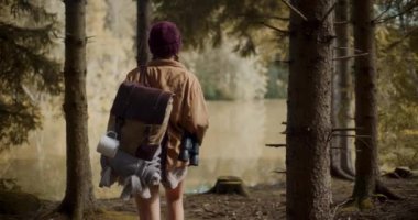 Sırt çantalı kadın turist, tatil sırasında ormanda göl kenarında keşif yapıyor.