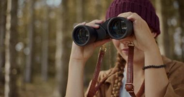 Yaz tatilinde ormanı keşfederken dürbünle bakan genç bir kadın.