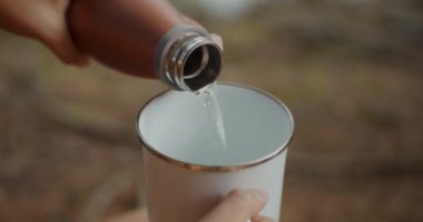 Kırpılmış kadın elleri ormanda şişeden bardağa su döküyor.
