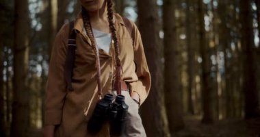 Sırt çantalı ve dürbünlü genç bir kadın yaz tatilinde ormanda keşif yapıyor.