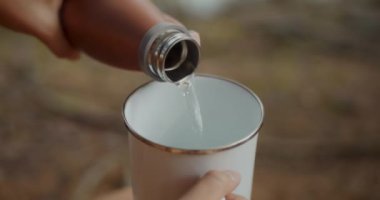 Kırpılmış kadın elleri ormanda şişeden bardağa su döküyor.