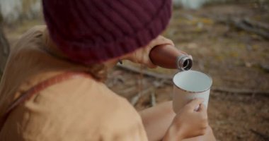 Genç bayan kaşif yaz tatilinde ormanda otururken bardaktan bardağa su dolduruyor.