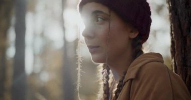 Düşünceli, genç bayan kaşif örgü şapkalı, tatilde ormana bakıyor.