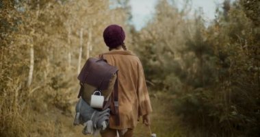 Sırt çantası ve şişesiyle ormanda ağaçların arasında yürüyen genç bir kadın turist.