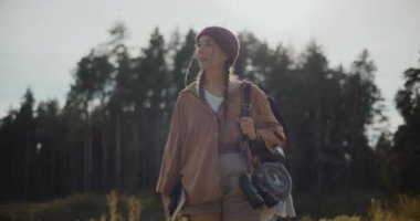 Gülümseyen genç bayan kaşif güneşli bir günde ormanı keşfederken etrafına bakıyor.