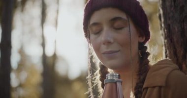 Tatil sırasında ormanda örülü şapka ve açık şişe giyen genç bir kadın.