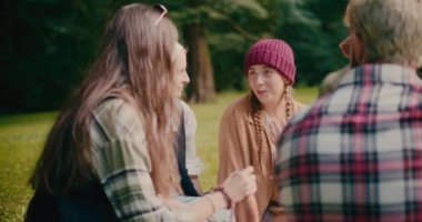 Örgü şapka takan genç bir kadın ormanda piknik yaparken arkadaşlarıyla eğleniyor.