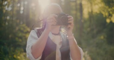 Gülümseyen kadın yürüyüşçü tatil sırasında ormanda kamera ile fotoğraf çekiyor.
