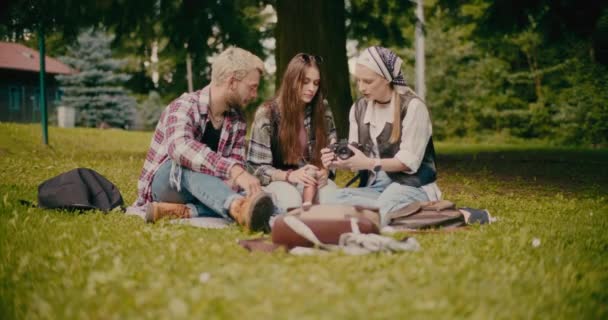 公園で草の上に座っている間 カメラについて友達に教える若い女性 — ストック動画