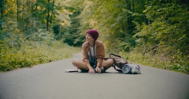 Беззаботная Молодая Туристка Сидит Скрещенными Ногами Вытянутыми Дороге Лесу — стоковое видео