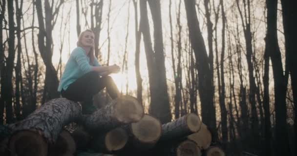 Улыбающаяся Молодая Женщина Рукой Подбородке Сидит Сложенных Бревнах Лесу Закате — стоковое видео