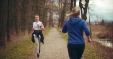 Formda sporcu kadın, bayan arkadaşına el sallıyor ve parkta egzersiz yaparken koşuyor.