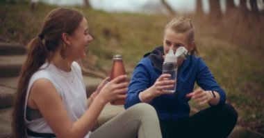 Antrenmandan sonra bahçede dinlenirken kız arkadaşıyla su şişesini kızartan mutlu kadın.