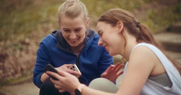 Neşeli Genç Bayan Sporcular Bahçede Otururken Cep Telefonu Kullanıyor Gülüyorlar — Stok video