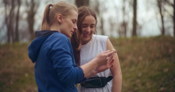 Jovem Loira Compartilhando Telefone Celular Com Sorridente Amigo Feminino Parque — Vídeo de Stock