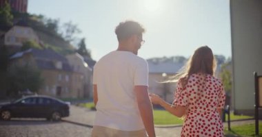 Güneşli bir günde yaya yolunda yürürken konuşan genç çiftin arka görüntüsü.