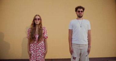 Duvarda dururken güneş gözlüğü takan genç bir çift.