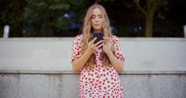 Genç bir kadın duvarın önünde dururken cep telefonuna mesaj atıyor.