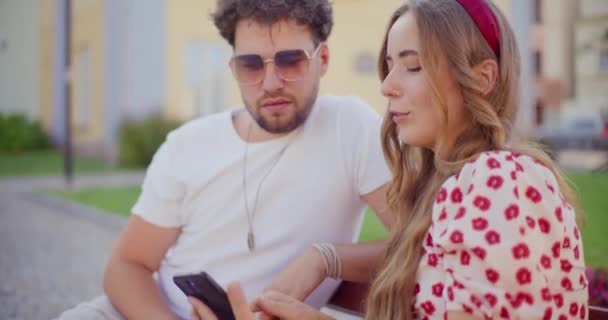 ブロンドの女性は スマートフォンを共有し 庭に座っている間に彼氏と話す — ストック動画