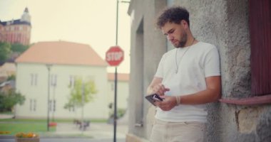 Genç adam gün batımında binaya karşı dururken akıllı telefon kullanıyor.