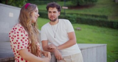 Genç adam kız arkadaşıyla konuşurken park duvarına yaslanıyor.