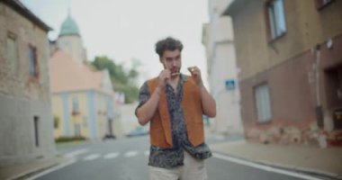 Kasabadaki evlerin arasında yol kenarında dururken güneş gözlüğü takan şık bir adam.