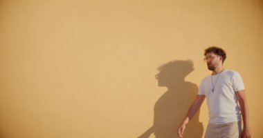 Yakışıklı genç adam duvarın önünde dururken güneş gözlüğünü çıkartıyor.