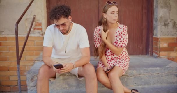 Mladý Muž Pomocí Mobilního Telefonu Sedí Blond Přítelkyně Proti Dveřím — Stock video