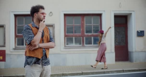 町の徒歩道に女性の友人と立っているヒップに手を持っている若い男 — ストック動画