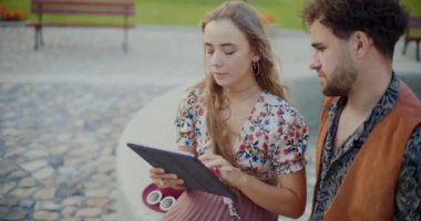Hafta sonu park yerinde erkek arkadaşının yanında dijital tablet kullanan sarışın genç bir kadın.
