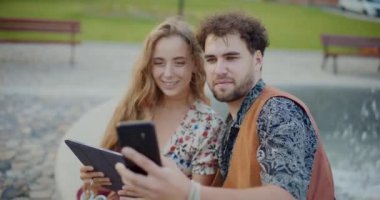 Genç adam, tatilde bahçede otururken akıllı telefonuyla kız arkadaşıyla selfie çekiyor.