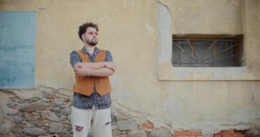 Kollarını kavuşturmuş yakışıklı genç adam. Kasabadaki binaya bakarken etrafına bakıyor.