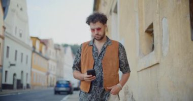 Genç adam akıllı telefondan mesajlaşıyor. Kasabadaki yaya yolunda yürüyor.