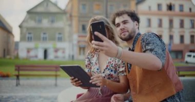 Genç adam hafta sonu parkta otururken kız arkadaşıyla cep telefonundan selfie çekiyor.