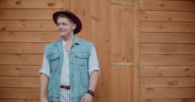 Ahşap duvarın karşısında dikilen şapkalı, gülümseyen yakışıklı adam.