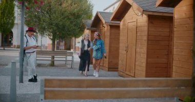 Genç adam cep telefonu kullanıyor. Direğe yaslanıyor. Yürüyen kadın arkadaşları tarafından.