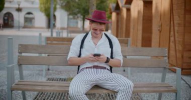 Gülümseyen yakışıklı adam bankta otururken akıllı telefondan mesaj atıyor.