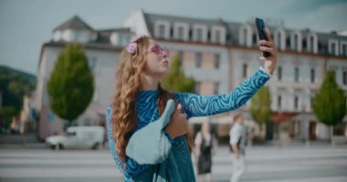 Kasabada cep telefonuyla selfie çekerken yüzünü buruşturan neşeli genç bir kadın.